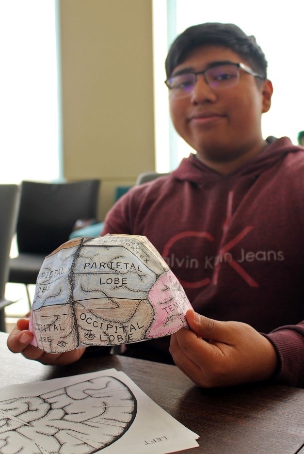 A photo of a student proudly displaying his handmade "brain hat."