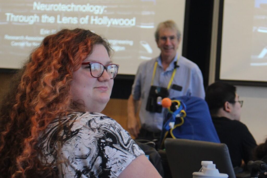 A photo of a student turning back to look at the camera, with the author Eric H. Chudler standing out of focus in front of her.